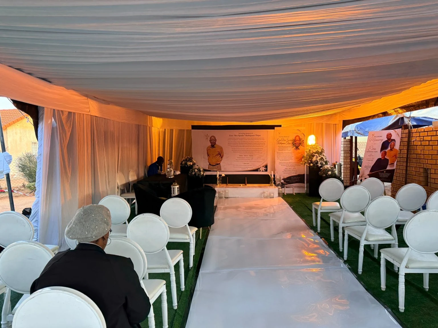 A wider view of the carefully dressed tribute venue: white seating, a central aisle and warm amber lighting.